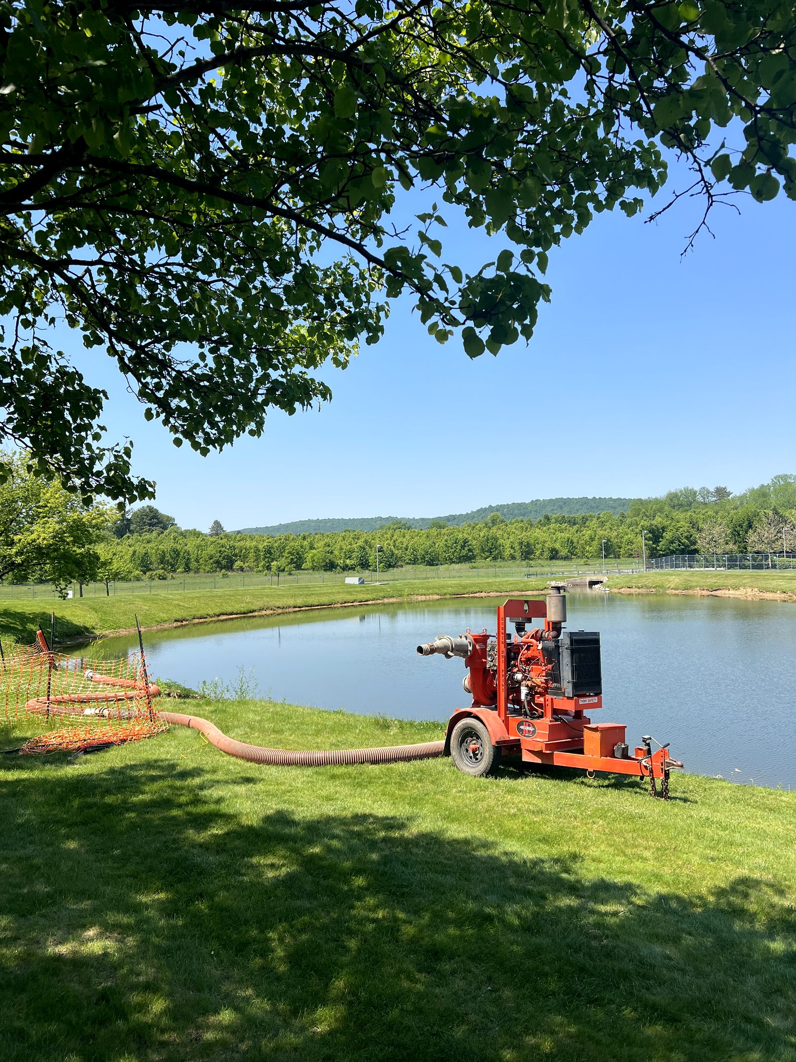 Orange basin pump running beside a pond under tree canopy at the Olympus project site