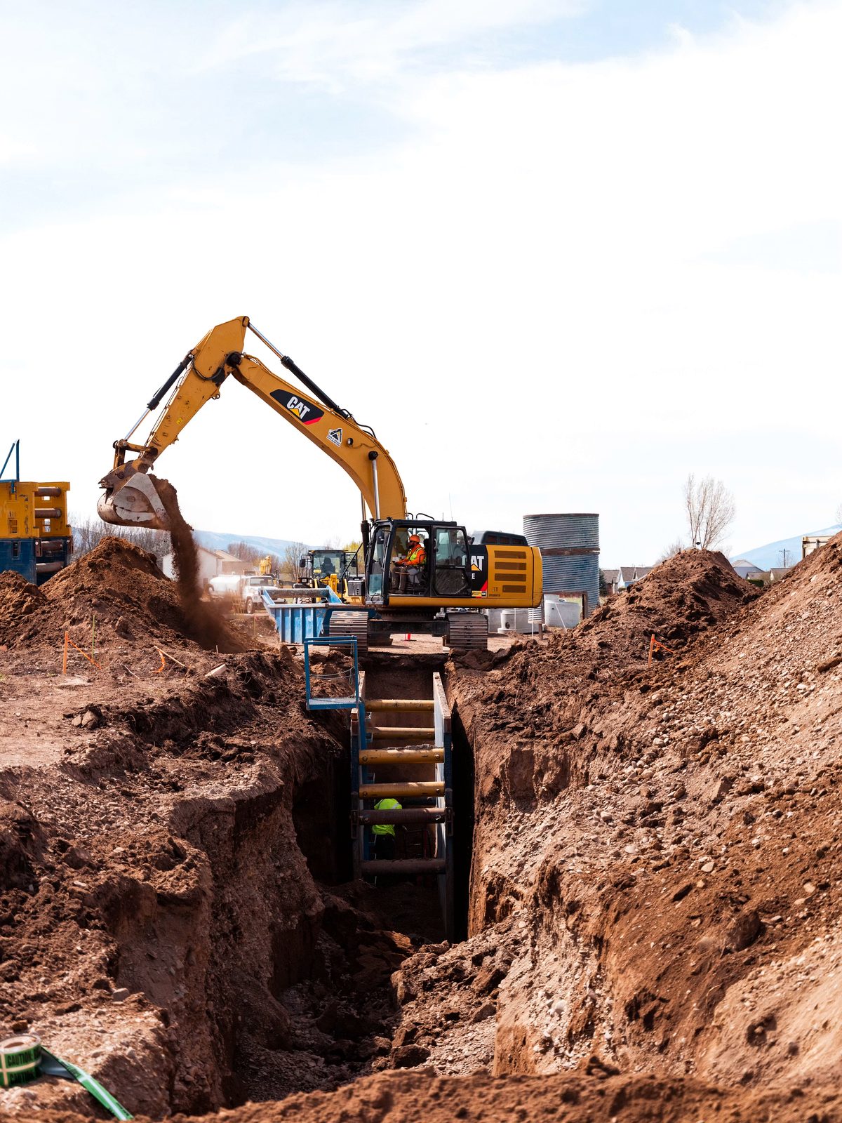 CAT excavator digging a red-earth utility trench